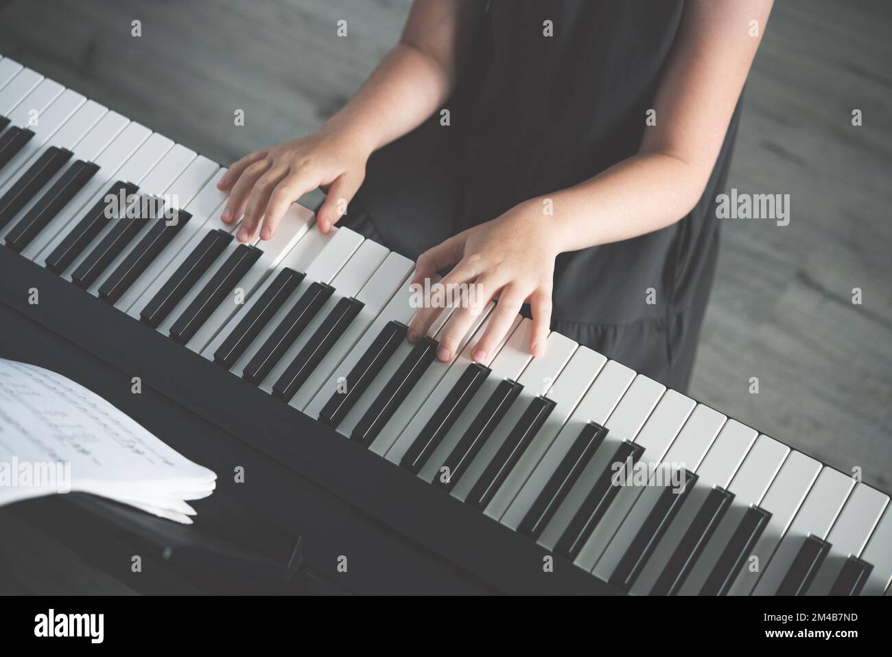 Le concept de développement des activités des enfants. Une fille dans une robe grise joue un piano électronique. Sans face. Vue de dessus et teinte de l'image Banque D'Images