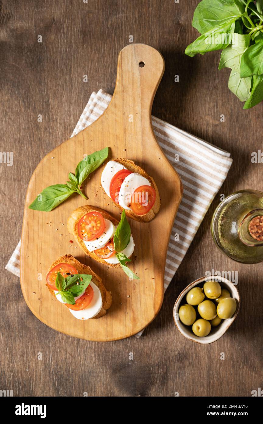 Sandwiches Caprese avec tomates fraîches, mozzarella et basilic frais et toast sur une planche à découper avec épices et huile d'olive sur un backgrou en bois Banque D'Images