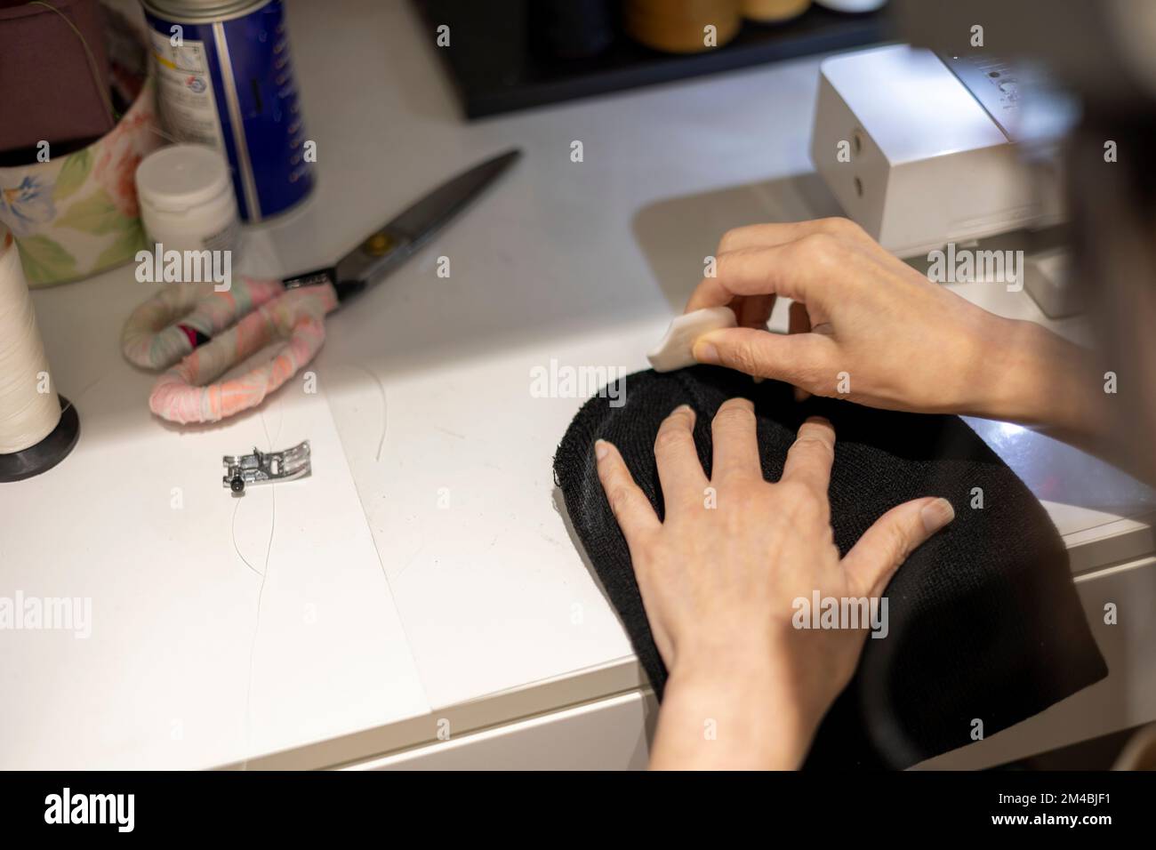 La femme est en train de coudre un bonnet beanie noir sur une machine à coudre, en utilisant une machine à coudre sur la table à coudre Banque D'Images