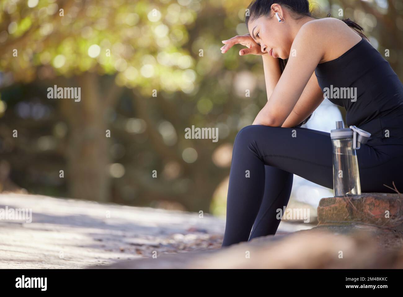 Fitness, fatiguée et femme dans un parc prenant une pause dans l'eau dans la nature pour écouter la radio ou la musique. Exercice, repos et la sueur de fille à respirer pendant Banque D'Images