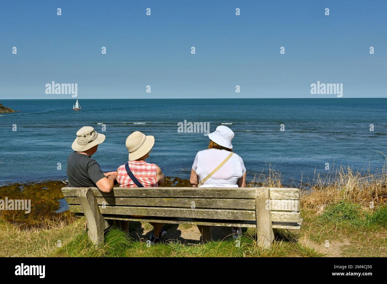 Newport, Pembrokeshire, pays de Galles - août 2022 : trois personnes assises sur un siège en bois prenant une pause d'une promenade le long du chemin côtier Banque D'Images