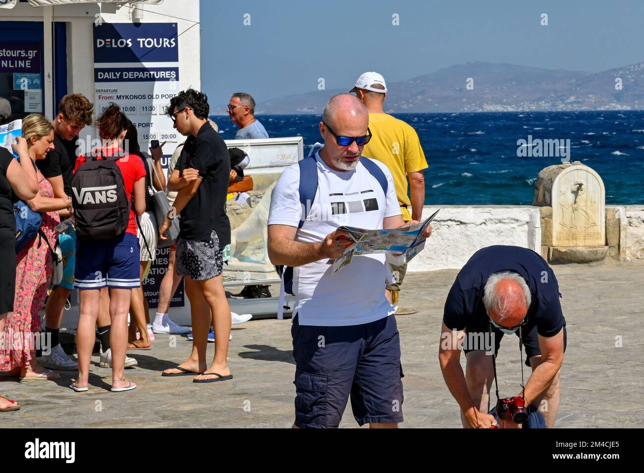 Mykonos, Grèce - juin 2022 : visiteur lisant une carte sur le front de mer du port après avoir débarqués d'un bateau de croisière Banque D'Images