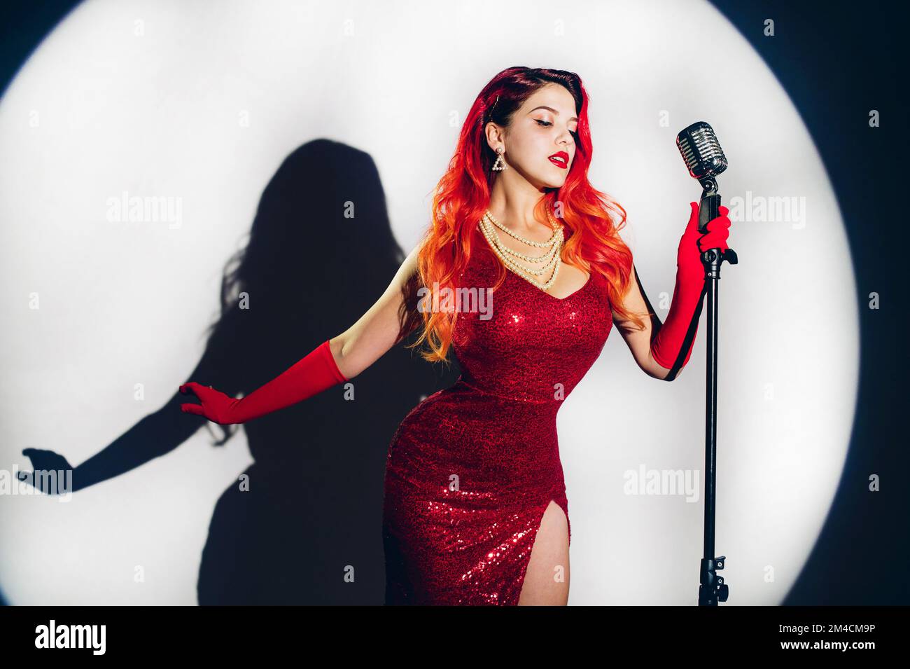 Jolie femme en robe rouge brillante avec un cheveux rouge tenant micropho Banque D'Images