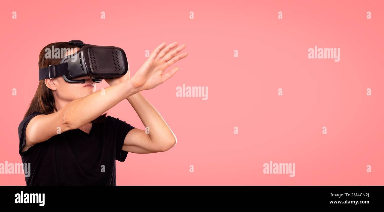 Femme portant un casque de réalité virtuelle, fond rose. Banque D'Images