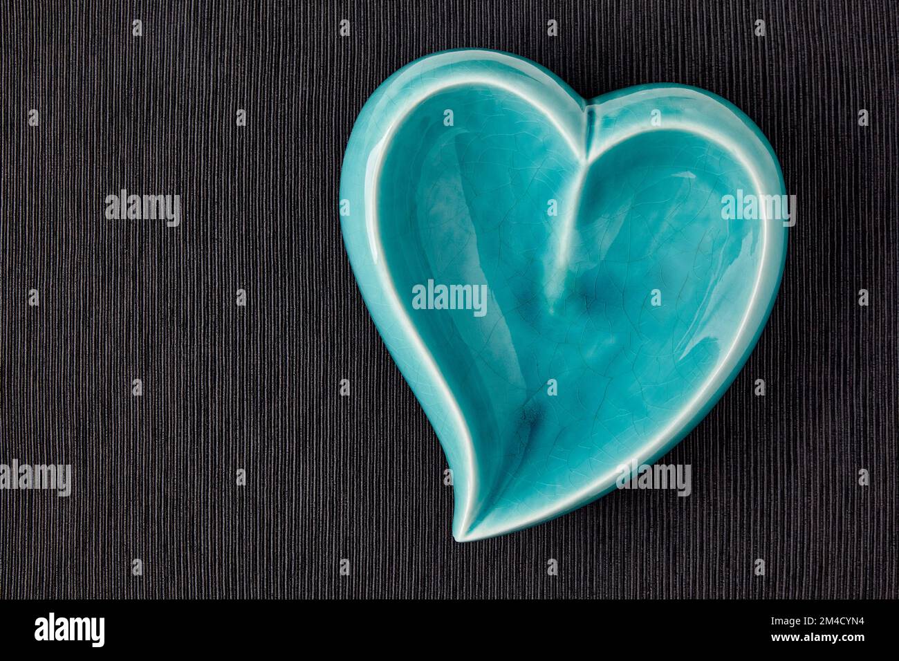 Bol en céramique bleu turquoise en forme de coeur sur une nappe en tissu noir Banque D'Images