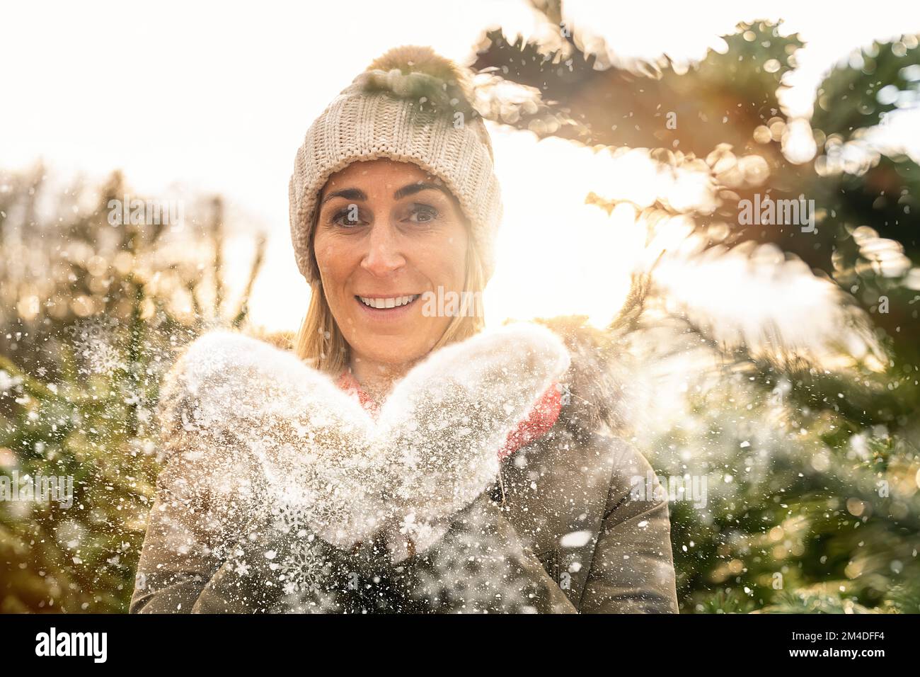 bonne femme en vêtements d'hiver soufflant de la neige lors d'une journée d'hiver enneigée à l'extérieur. Banque D'Images