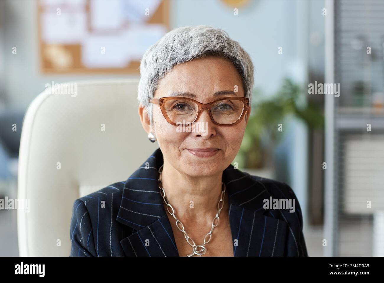 Portrait d'une femme âgée en tant que patron féminin assis sur le lieu de travail et souriant à l'appareil photo Banque D'Images