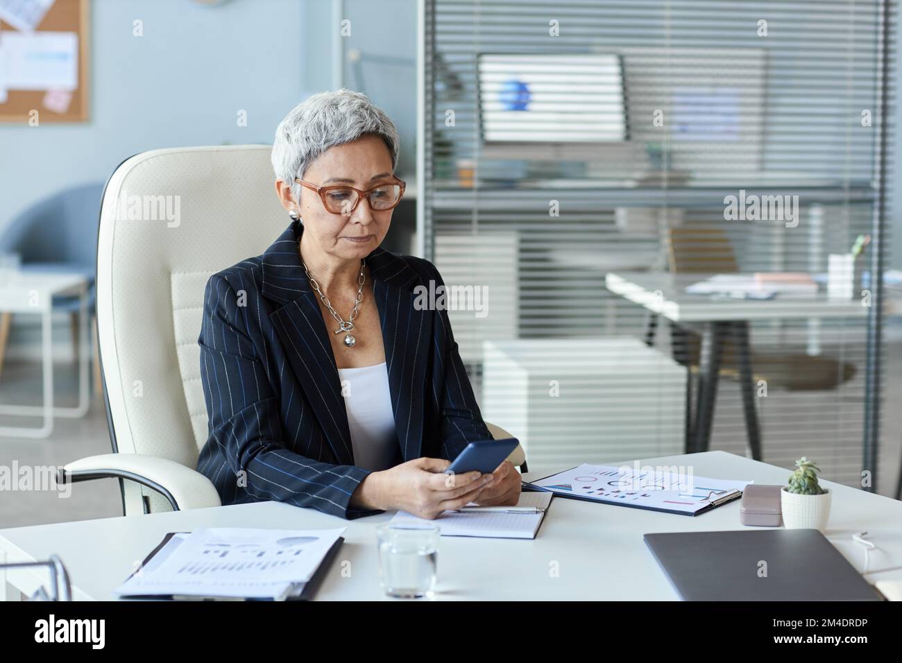 Portrait d'une femme âgée en tant que chef de sexe féminin, assise au bureau et utilisant un smartphone, espace de copie Banque D'Images