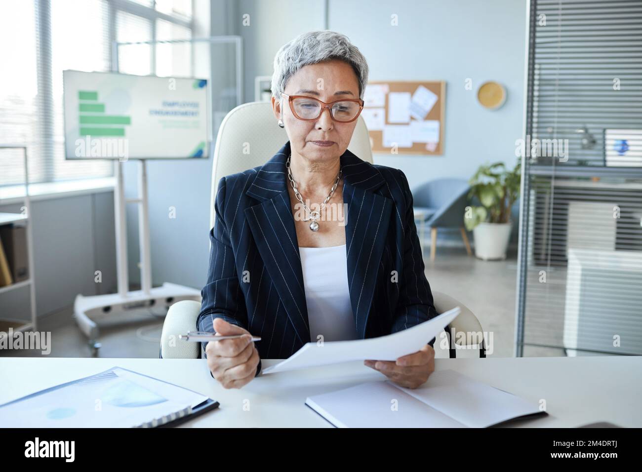 Portrait d'une femme âgée en tant que patron féminin assis au bureau et lisant un document Banque D'Images