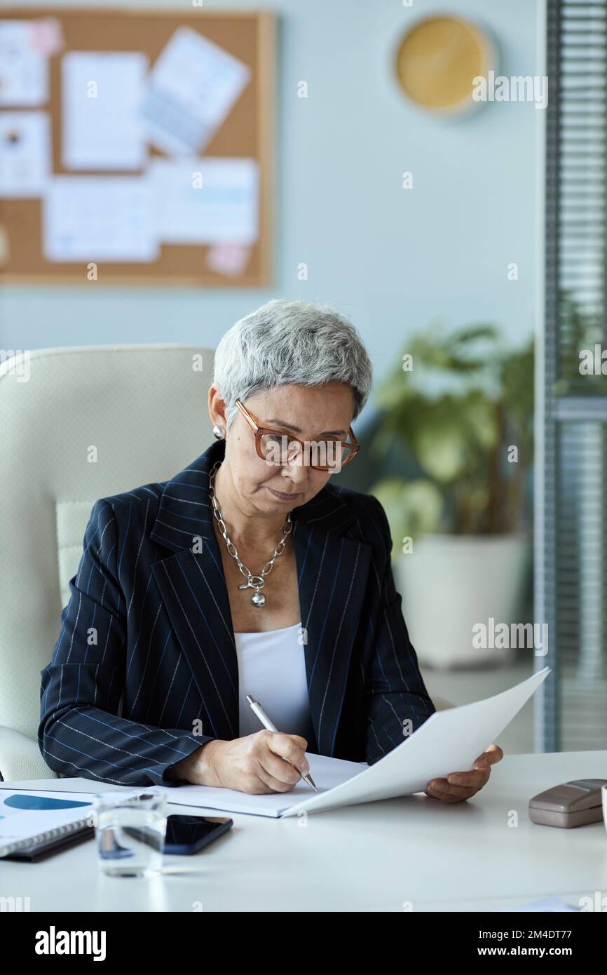 Portrait vertical de la femme âgée en tant que patron féminin lisant le document sur le lieu de travail au bureau Banque D'Images