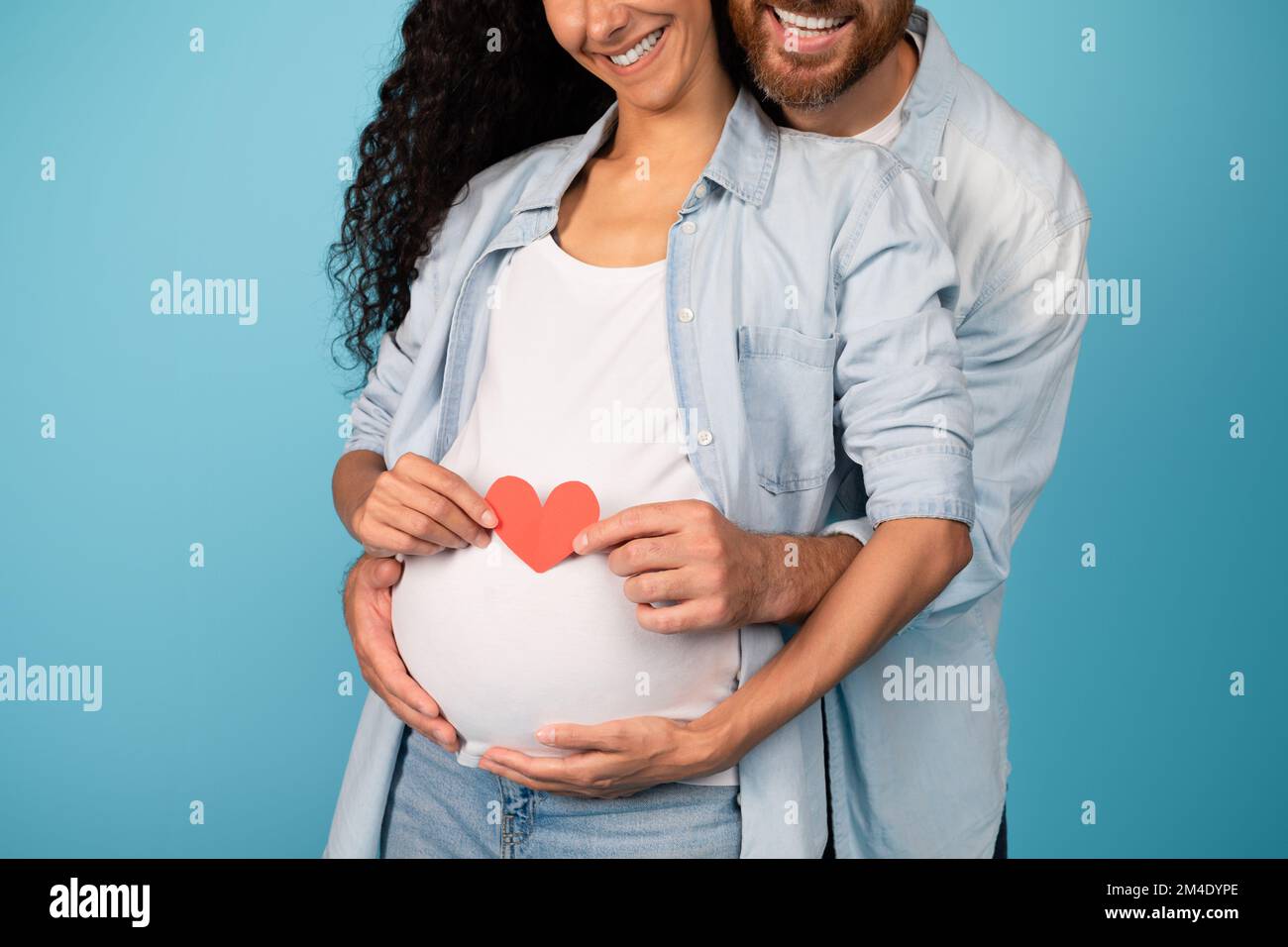 Souriant jeune européen mec embrassant femme enceinte dans décontracté tenant le coeur sur le grand ventre Banque D'Images