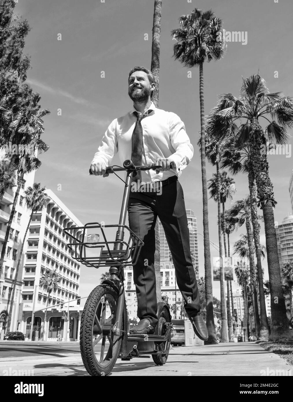 Un gars heureux en tenue de formalwear scooter électrique sur le trottoir, le démarrage Banque D'Images