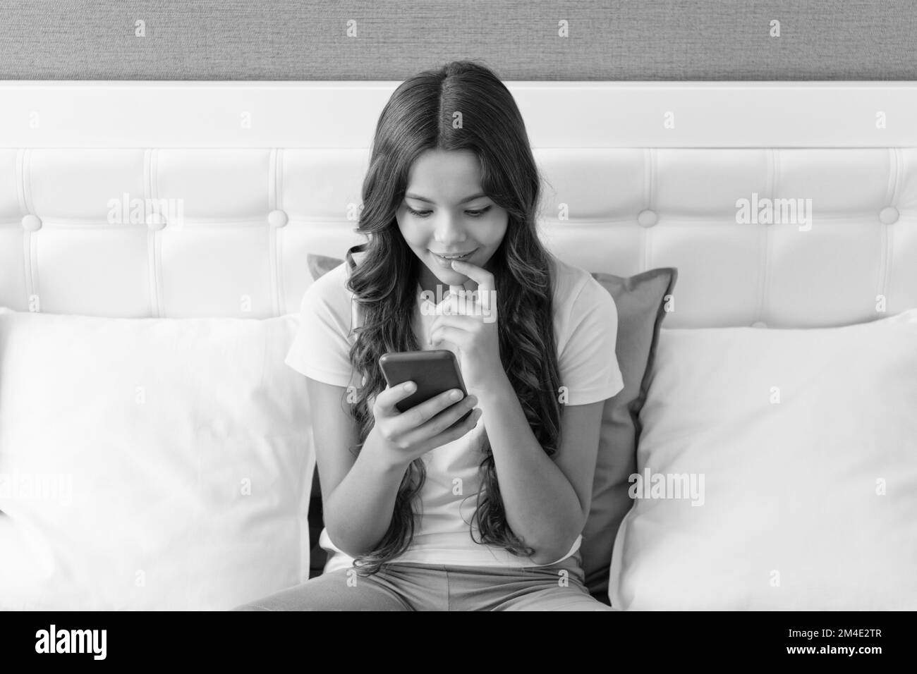 Génération de smartphones. Un enfant heureux utilise un téléphone intelligent assis sur le lit. Chat sur smartphone Banque D'Images