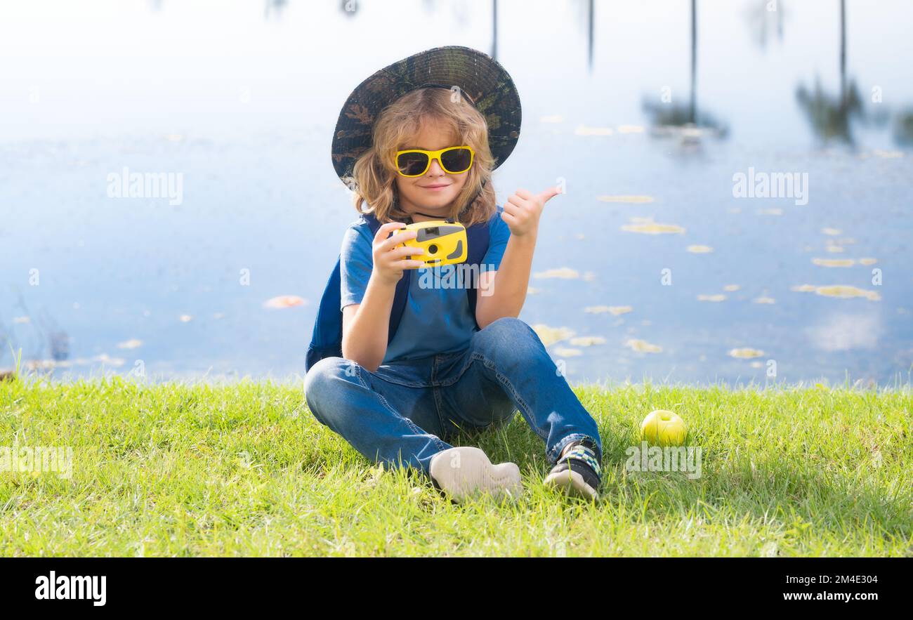 Enfant avec appareil photo voyageant à l'extérieur. Garçon voyageur avec sac à dos dans une journée d'été. Portrait d'un petit garçon explorant la faune. Randonnée et aventure Banque D'Images