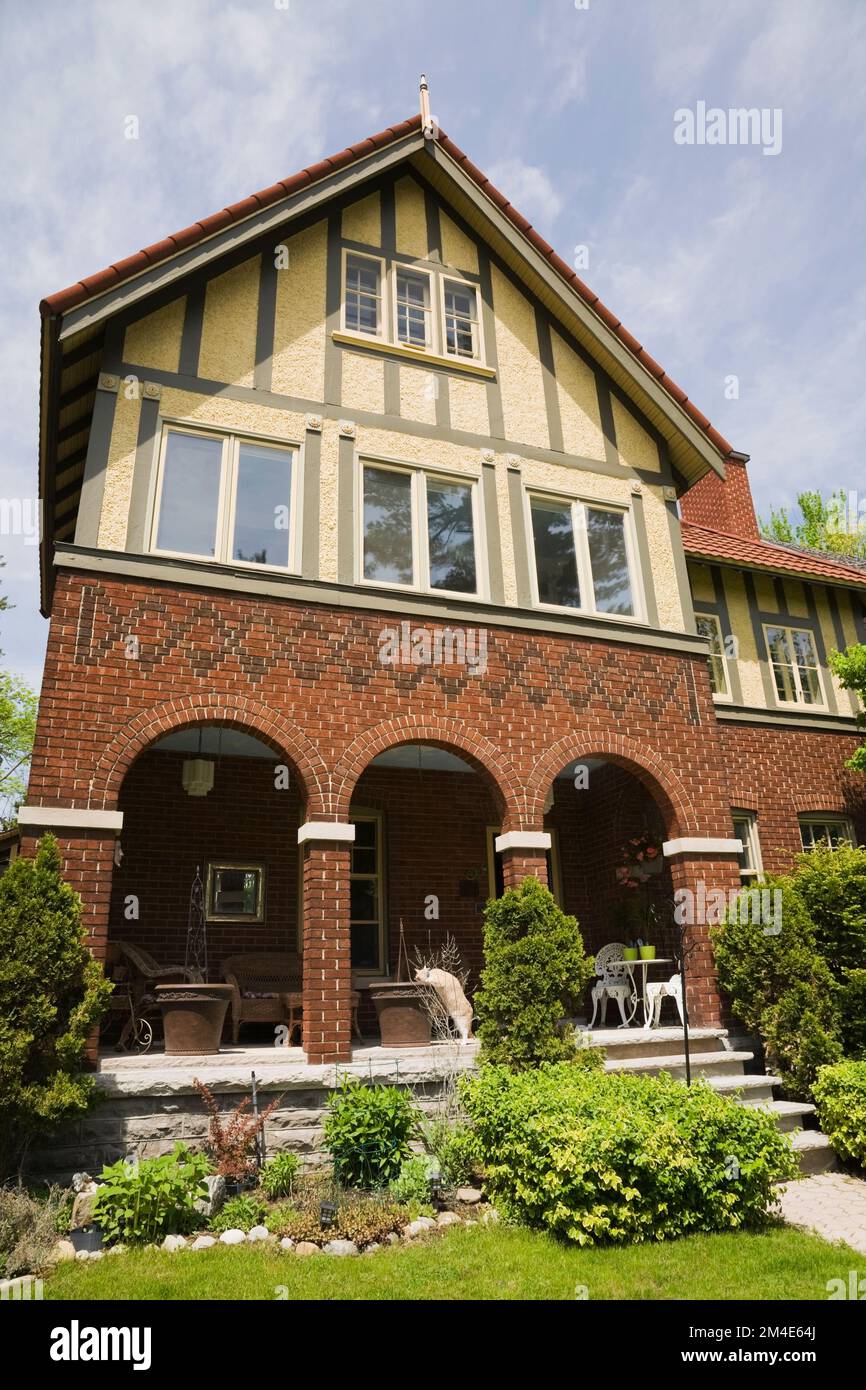 Briques rouges brunes et stuc beige avec garniture vert olive style Tudor maison de style cottage avec cour avant paysagée au printemps. Banque D'Images