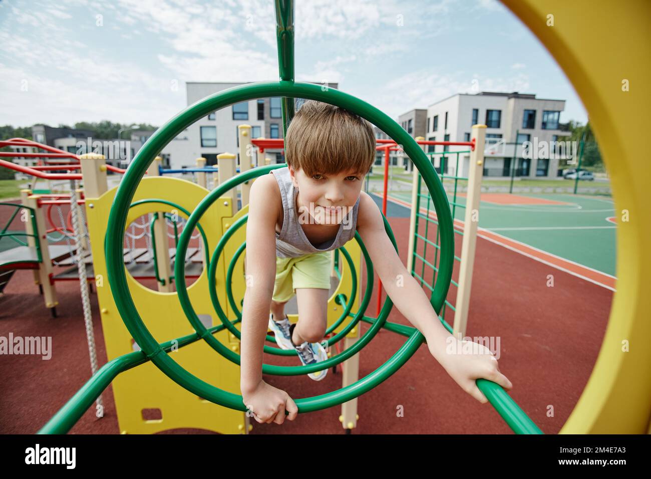 Portrait d'un garçon jouant dans la jungle gym sur un terrain de jeu coloré et regardant l'appareil photo, espace de copie Banque D'Images