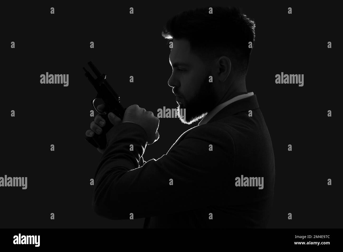Silhouette de jeune homme en costume avec pistolet sur fond sombre Banque D'Images
