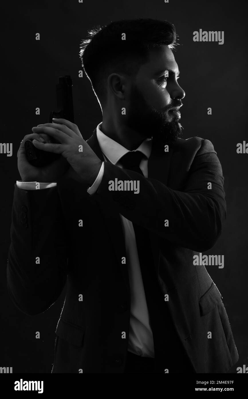 Silhouette de jeune homme en costume avec pistolet sur fond sombre Banque D'Images