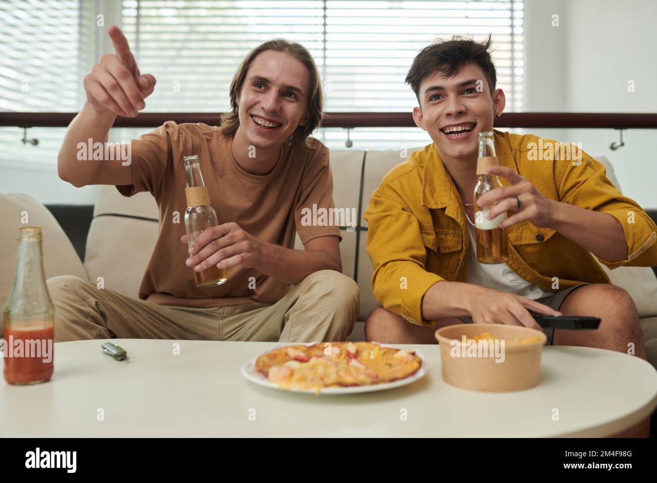 De jeunes hommes joyeux boivent de la bière en regardant un match de football à la maison Banque D'Images