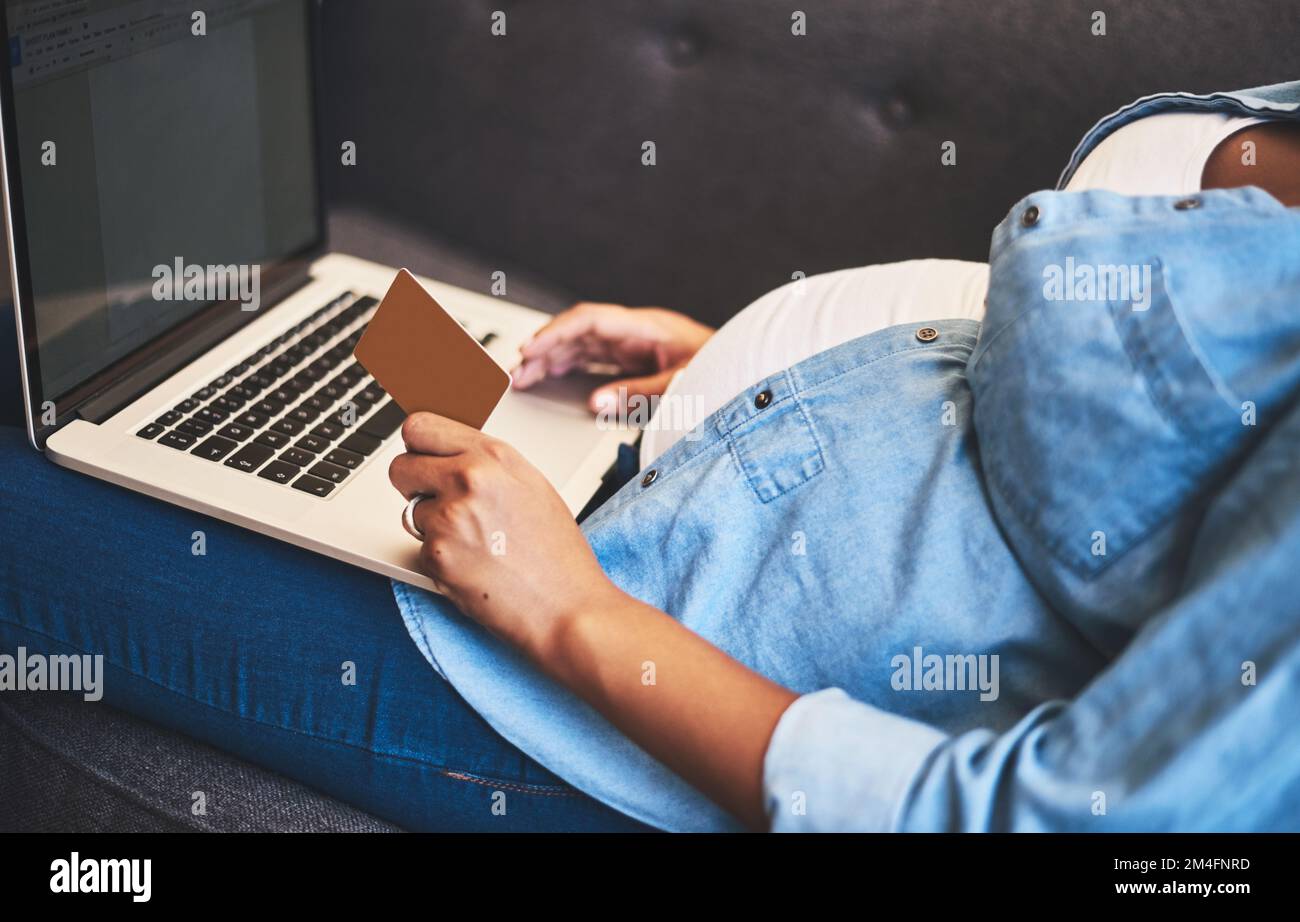 À l'approche de sa date d'échéance, elle déchite les files d'attente. une femme enceinte utilisant un ordinateur portable et une carte de crédit sur le canapé à la maison. Banque D'Images