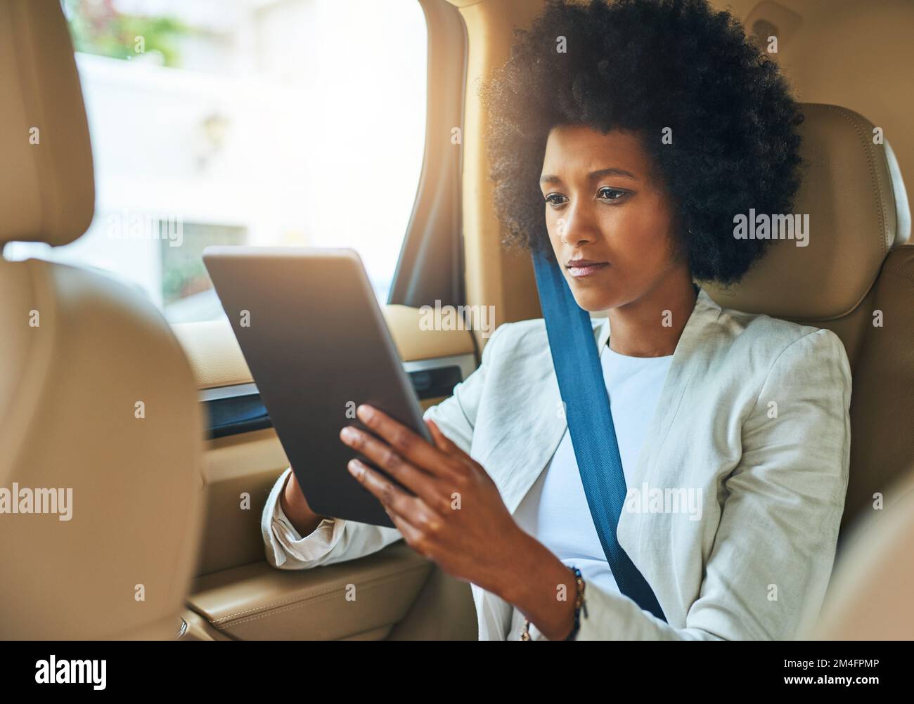 Toujours préparé avant le travail. une jeune femme d'affaires très concentrée s'est occupée de naviguer sur sa tablette numérique tout en étant assise à l'arrière d'une voiture en chemin Banque D'Images