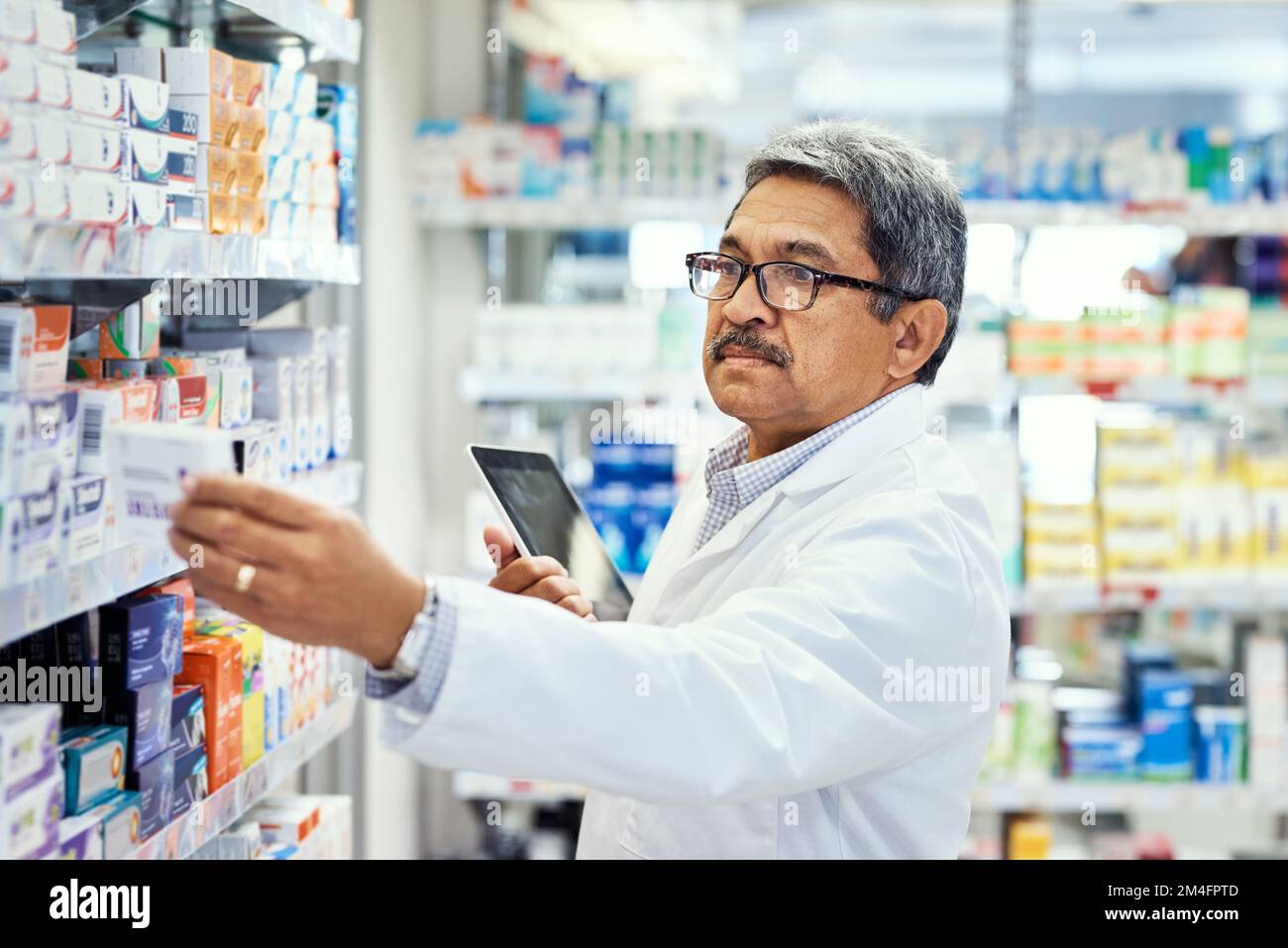 Décider du nouveau stock à commander. un pharmacien mature utilisant une tablette numérique tout en travaillant dans un chimiste. Banque D'Images