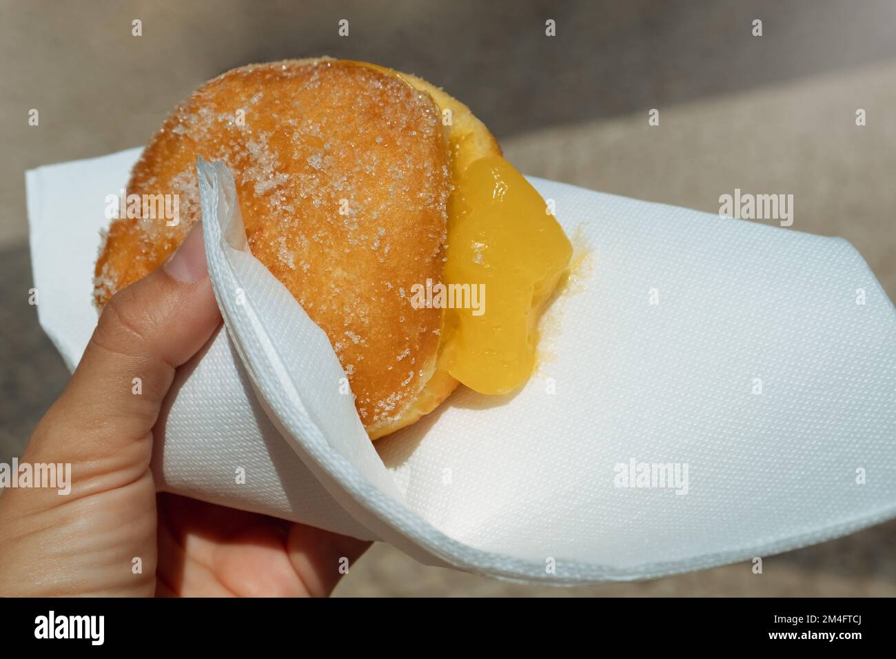 Main tenant Bola de Berlim ou Berlim ball, une pâtisserie portugaise faite à partir d'un beignet frit rempli de crème d'éggy douce et roulé dans du sucre croquant Banque D'Images