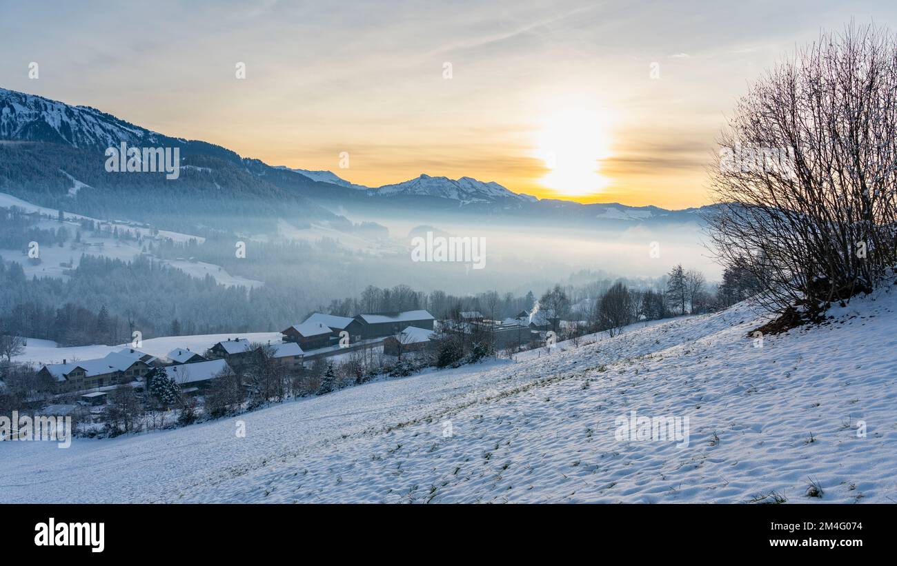 Betrieb einer Schneeinschaft, Schnee auf Wiese, Dorf, einzelner Baum und die Berge des Bregenzerwald im hintergrund. Abendsonne über Hittisau Banque D'Images
