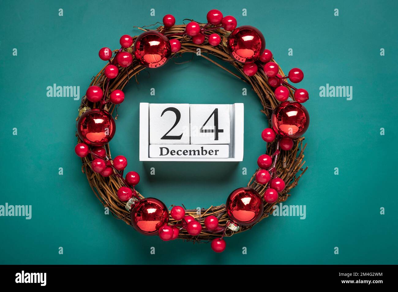 Couronne de Noël décorée de baies rouges, calendrier en bois date 24 décembre isolé sur fond vert concept de préparation de Noël, atmosphère voeux carte fait main couronne de Noël plat Lay. Banque D'Images