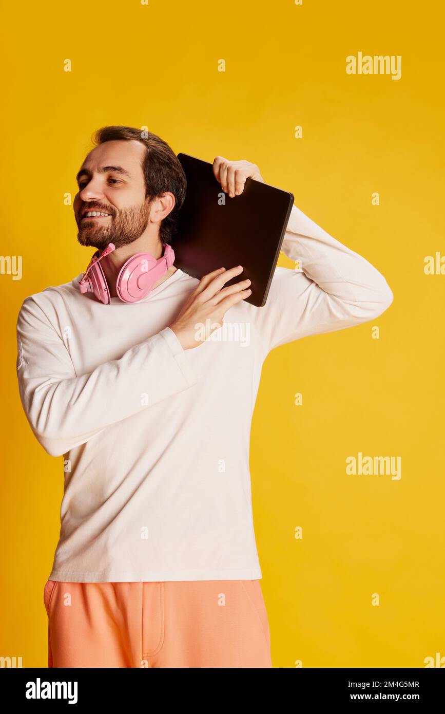 Homme mûr et charmant avec une barbe en vêtements décontractés tenant une tablette numérique isolée sur fond jaune. Concept de mode de vie actif, positif Banque D'Images