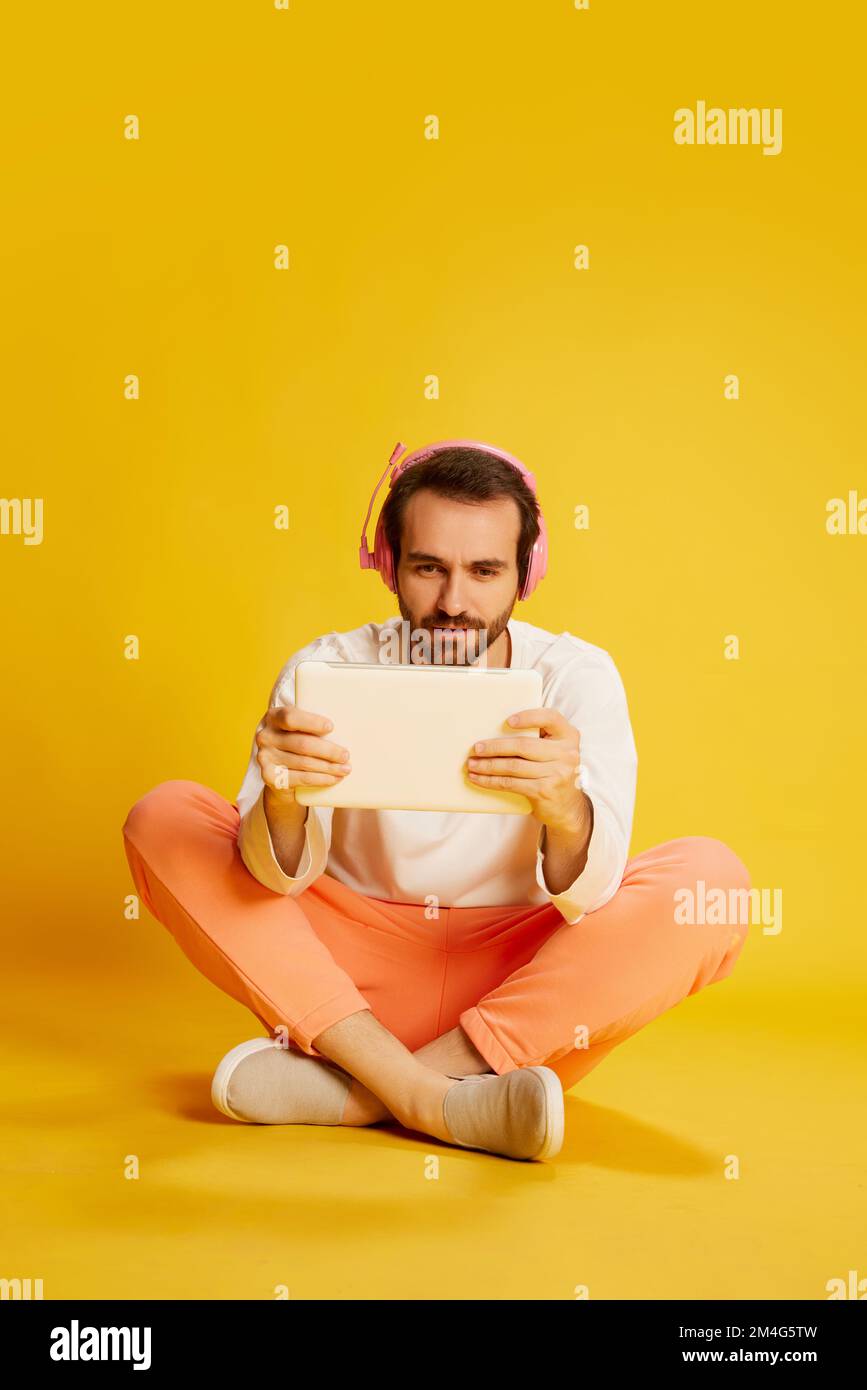 Étude à distance. Homme mûr et beau avec barbe en vêtements décontractés regardant la tablette isolée sur fond jaune. Concept de mode de vie actif Banque D'Images