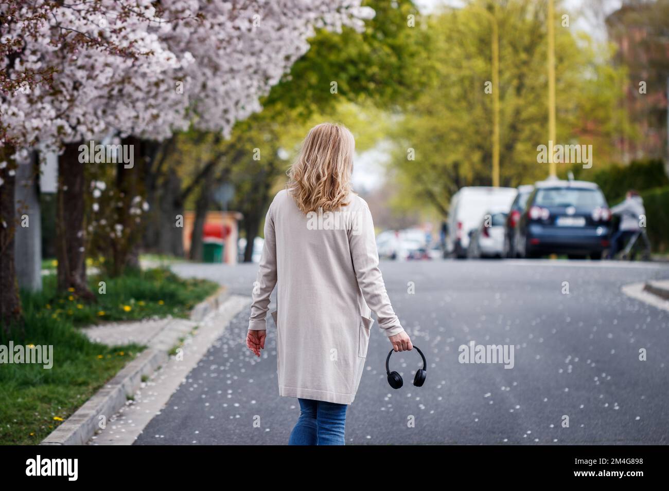Femme avec un casque marchant dans la rue de la ville sous les cerisiers en fleurs. La vie urbaine au printemps Banque D'Images