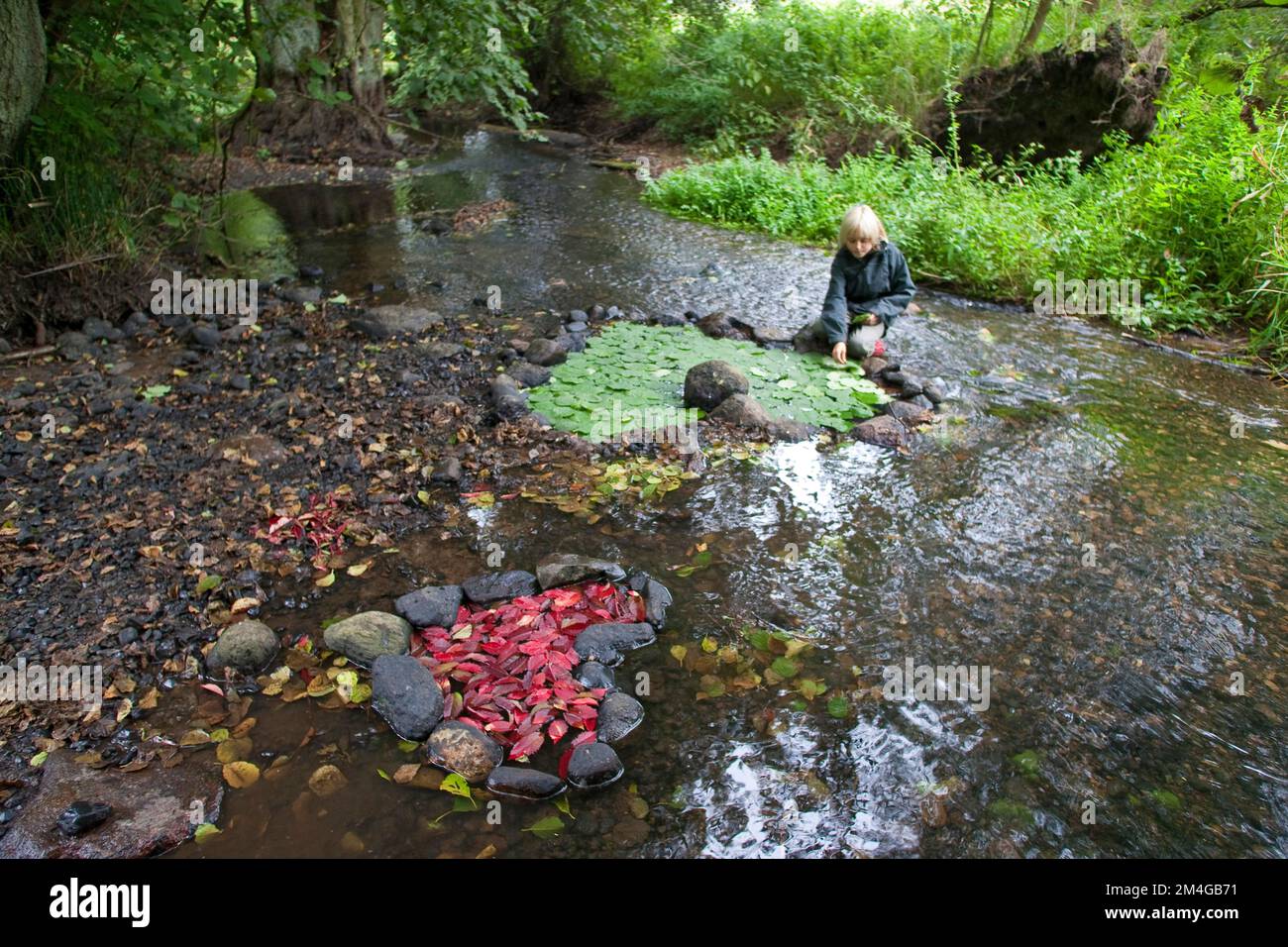 Enfant ont formé un coeur avec des pierres dans un ruisseau et rempli avec le rouge et le vert des feuilles, Allemagne Banque D'Images