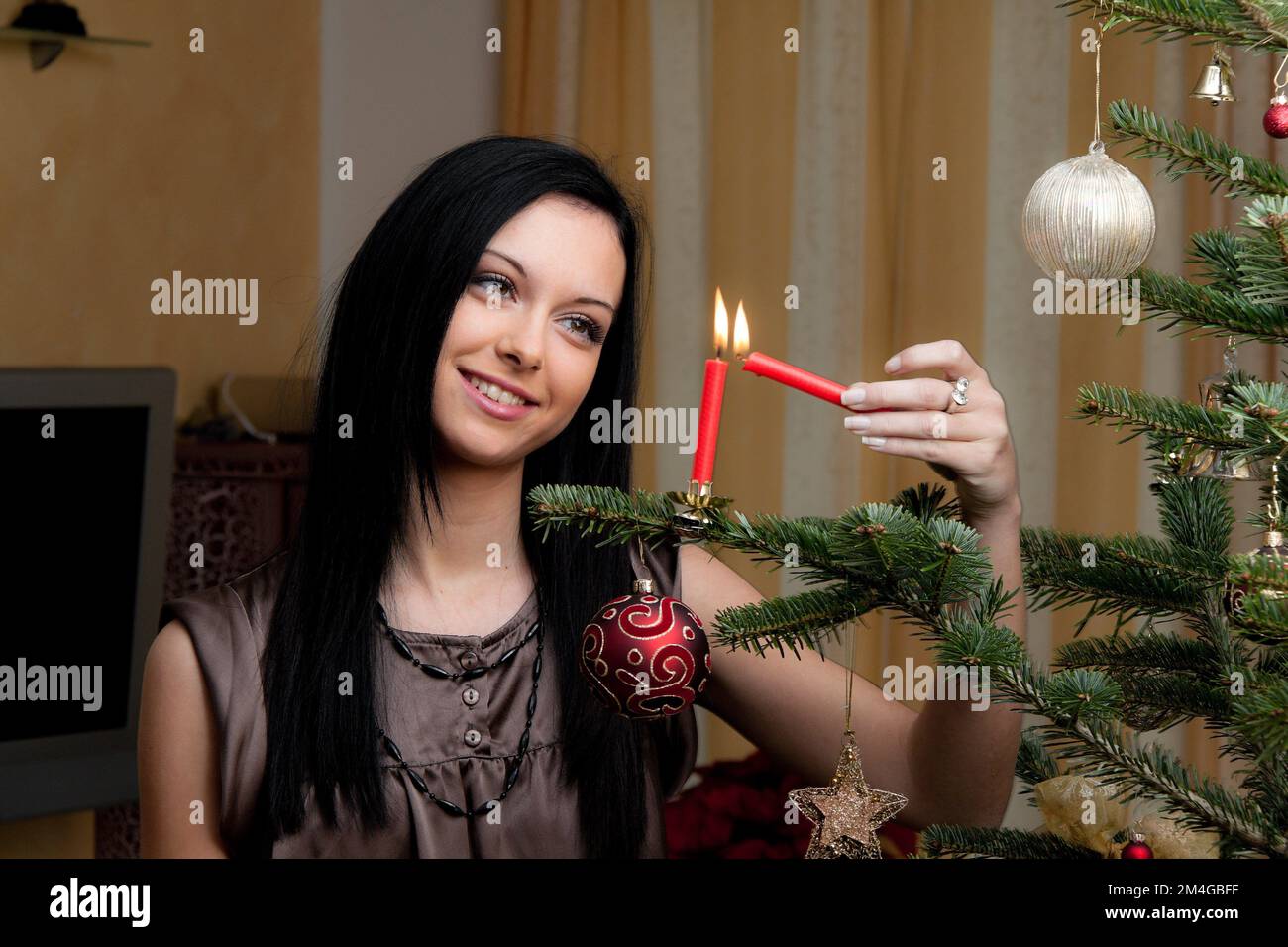 Jeune femme allumant les bougies sur l'arbre de Noël Banque D'Images