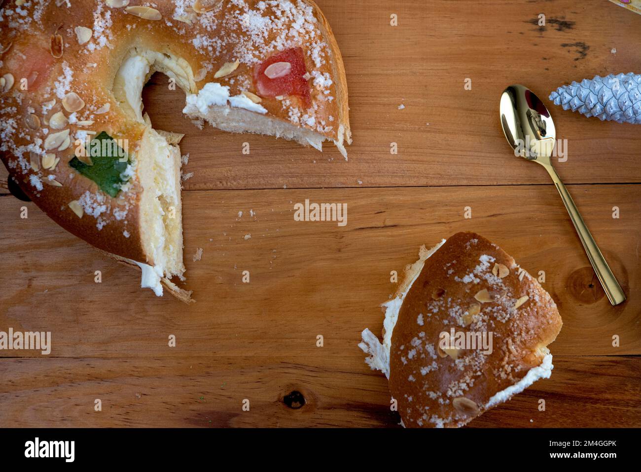 Roscon de reyes farci de crème, petit pain ou gâteau typique de l'Espagne le trois Kings Day avec une portion sur une assiette noire et fond noir. Banque D'Images