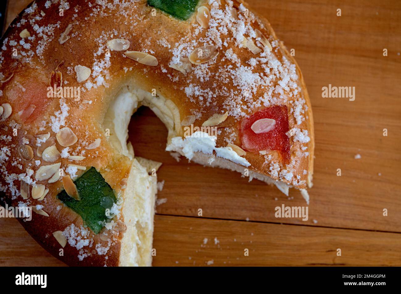 Roscon de reyes farci de crème, petit pain ou gâteau typique de l'Espagne le trois Kings Day avec une portion sur une assiette noire et fond noir. Banque D'Images