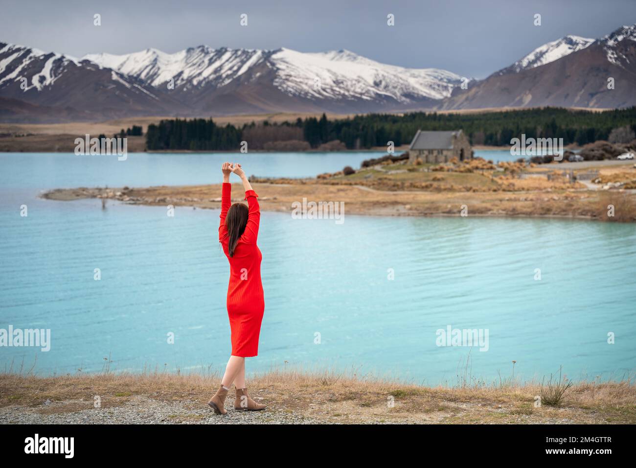 Une femme asiatique pose touristique à la couleur turquoise du lac Tekapo avec des sommets enneigés des alpes du sud de la Nouvelle-Zélande à l'arrière-plan. Banque D'Images