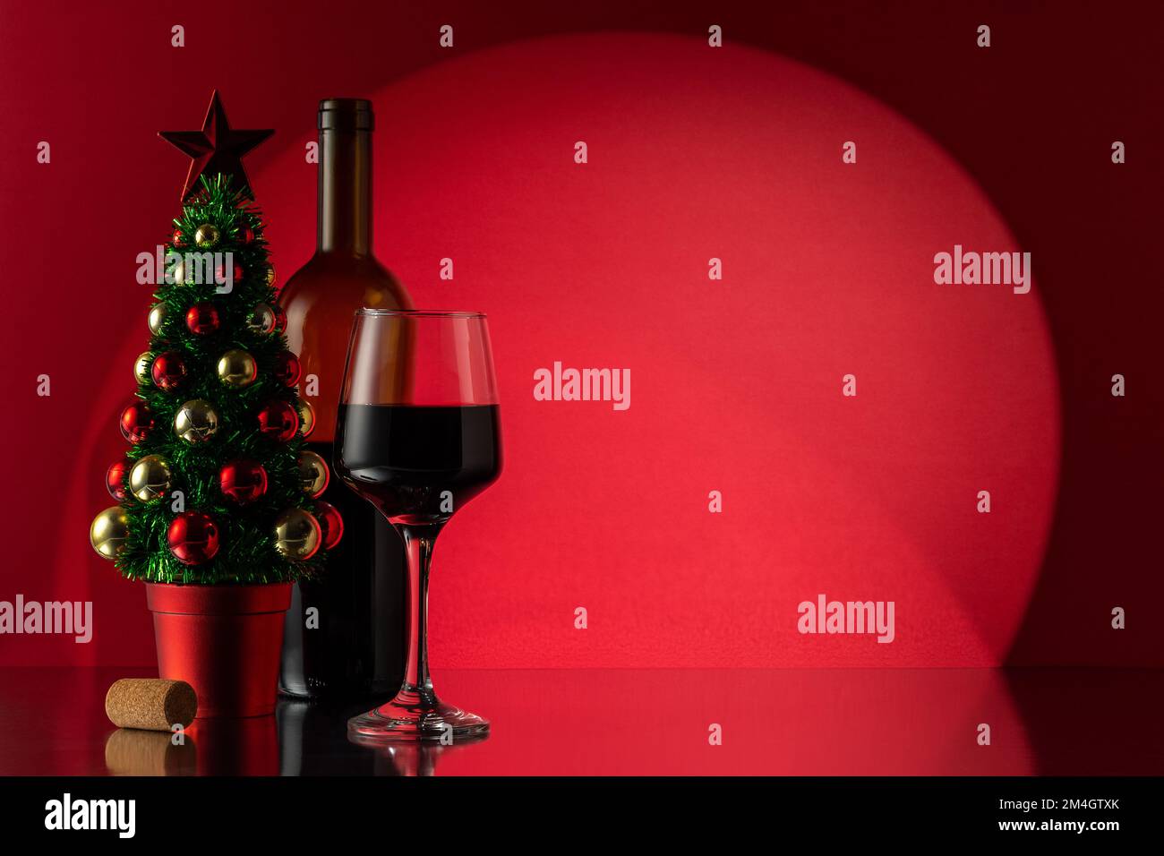 Bouteille de vin rouge, verre de vin et arbre de Noël devant le mur rouge. Nouvel an ou arrière-plan de Noël. Banque D'Images