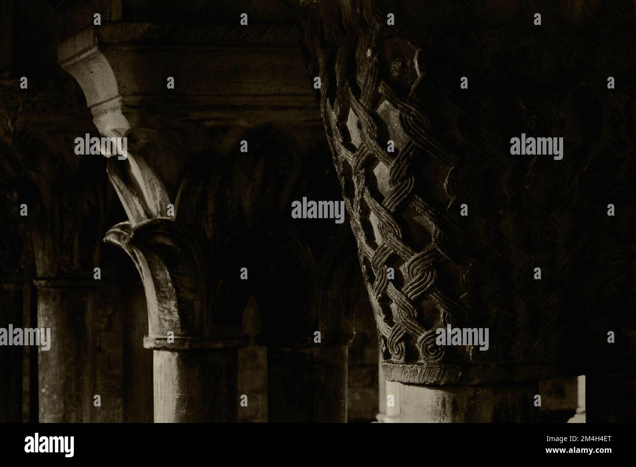 Vue sépia de l'entrelacement et du feuillage florissant sculptés par des pierres médiévales sur les capitales des colonnes doubles bordant les promenades ou les galeries du cloître roman de 1100s attaché à la cathédrale notre-Dame de Saint-Bertrand-de-Comminges, haute-Garonne, Occitanie, France, une ancienne cathédrale catholique romaine, maintenant une église paroissiale, C'est aussi la cathédrale Sainte-Marie. Banque D'Images