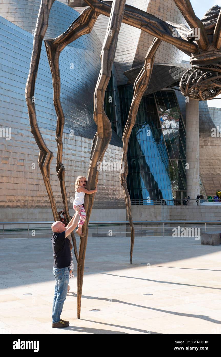 Une jeune fille qui escalade une jambe d'araignée est aidée par un homme plus âgé du Musée Guggenheim, Bilbao, pays basque, Espagne, Europe. Banque D'Images