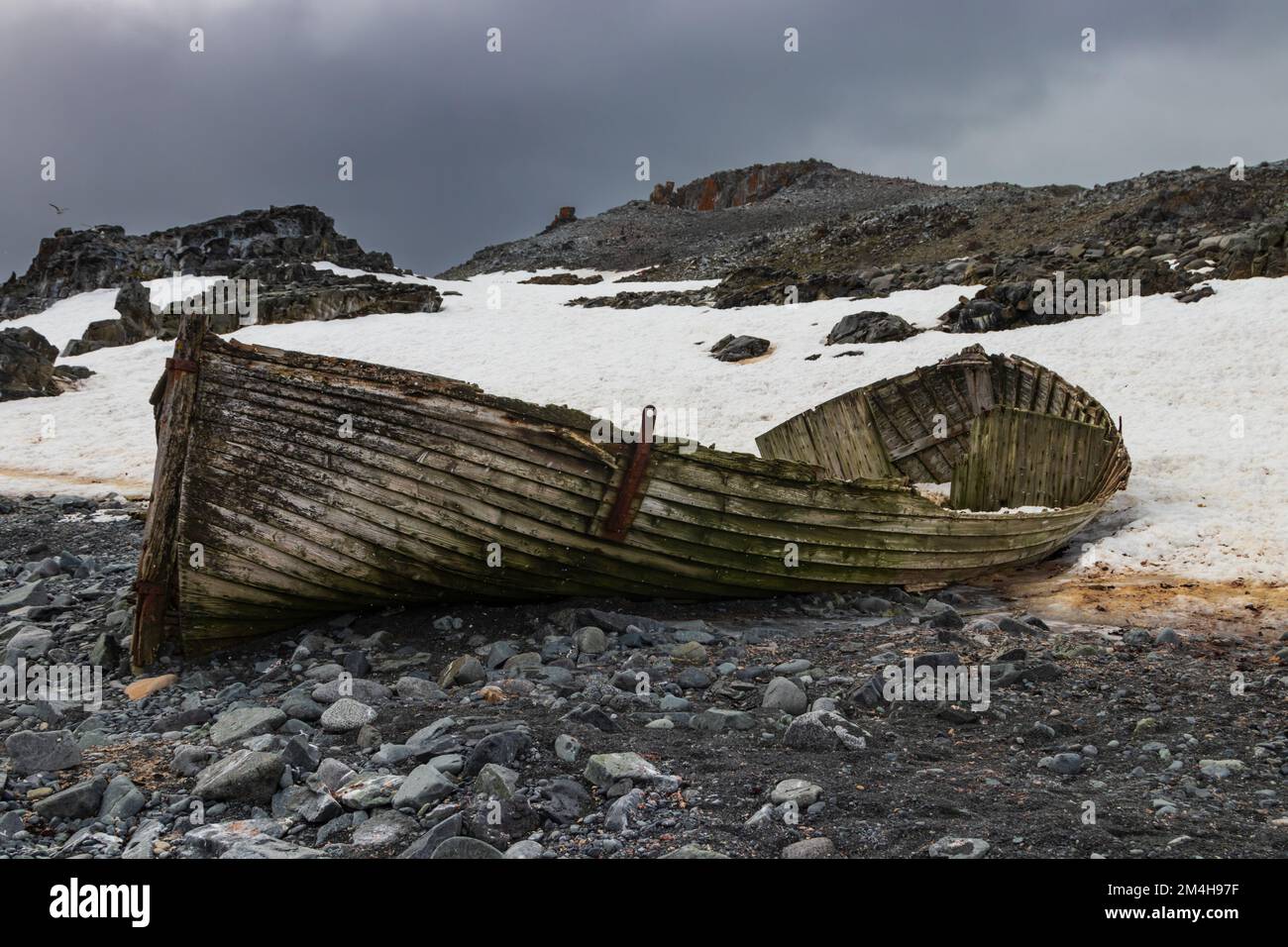 Vestiges d'un ancien bateau, sur la rive rocheuse de l'une des îles antarctiques. Péninsule. Neige, collines rocheuses en arrière-plan. Oiseaux et ciel nuageux. Banque D'Images