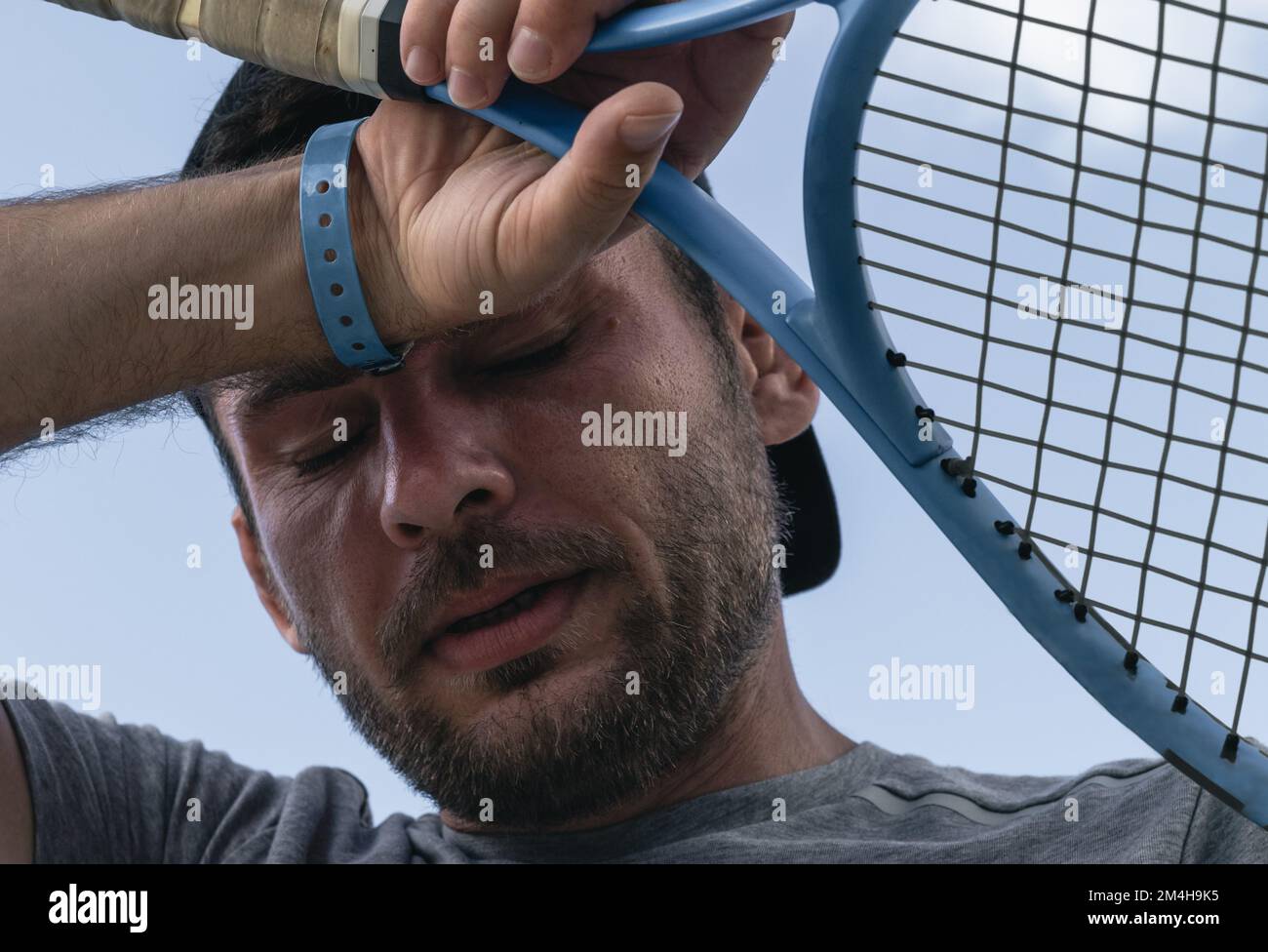 Portrait de la tête du joueur de tennis, l'athlète masculin tient la raquette de tennis dans sa main et élimine la sueur du front. Sportif fatigué, sportif et sain Banque D'Images