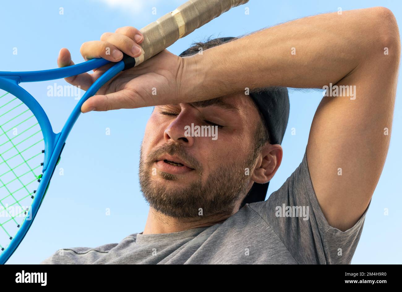 Homme barbu adulte joueur de tennis élimine la transpiration du front, photographie rapprochée de l'athlète fatigué après le match de tennis. Banque D'Images