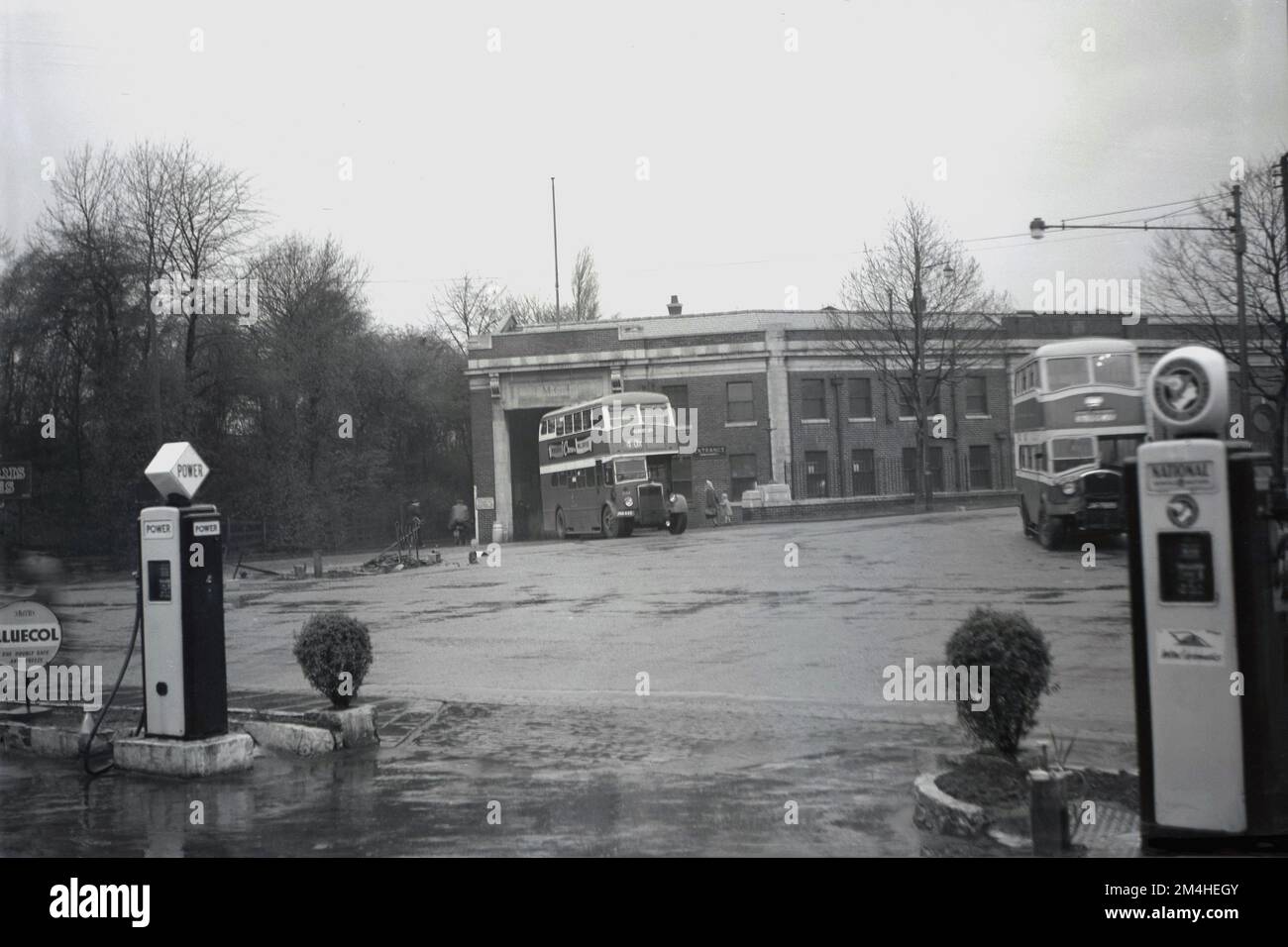 1950s, historique, vue depuis la piste de garage Hargood du dépôt d'autobus ou du terminus à Parrs Wood, Didsbury, Manchester, Angleterre, Royaume-Uni, Avec bus à impériale n° 40x en direction de la rue Albert Un signe pour Smith's Bluecol, l'antigel peut être vu, ainsi que les pompes à essence pour les marques de carburant de l'époque, Power et National. Banque D'Images