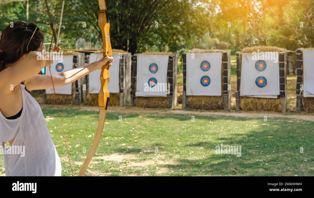 Hands of Woman vise l'arc de tir à l'arc et la flèche à la cible colorée dans le champ de tir pendant l'entraînement. Exercice et concentration avec tir à l'arc en plein air. Sélection Banque D'Images