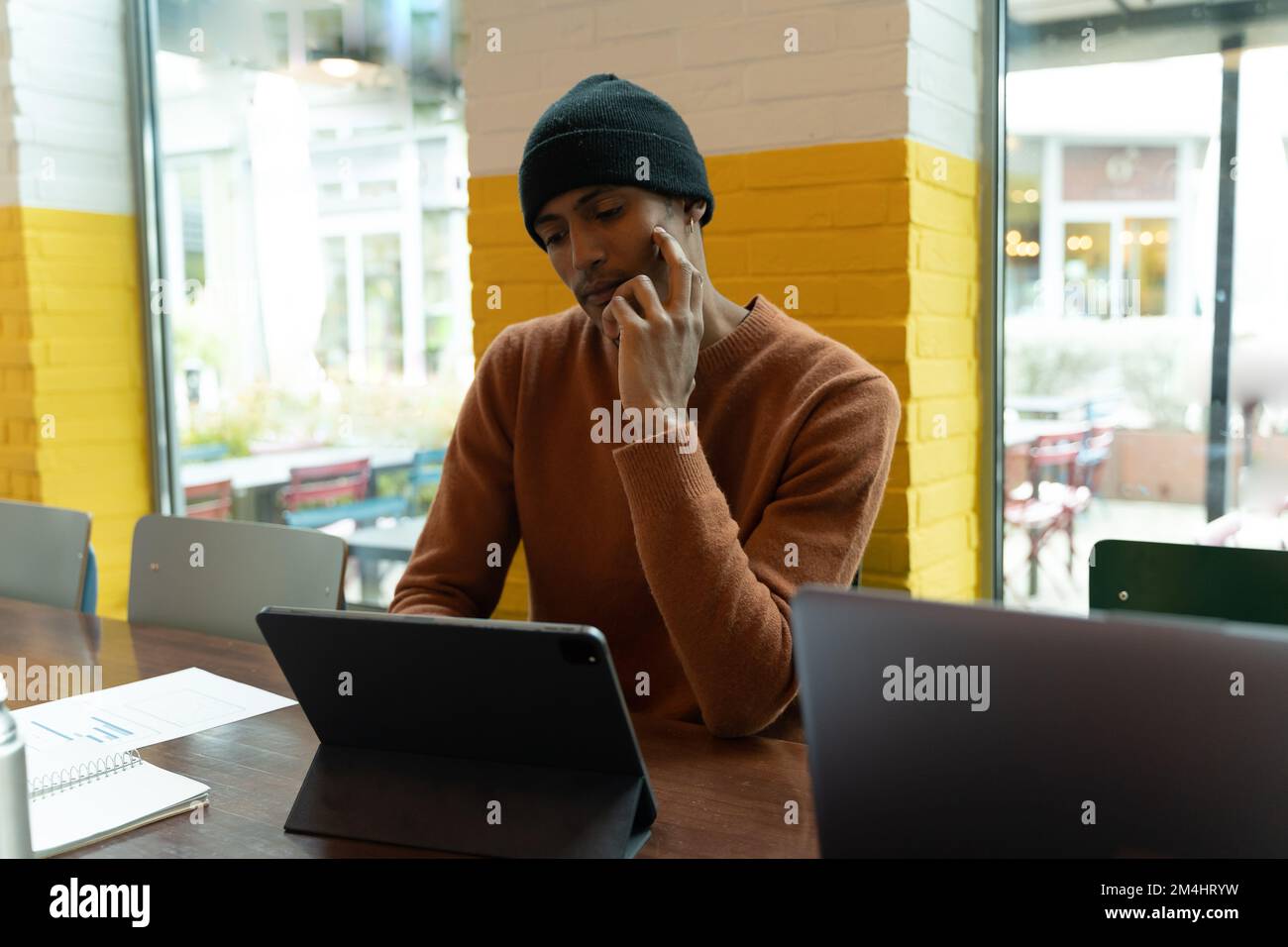 Jeune homme travaillant dans un espace de travail conjoint. Homme concentré regardant la tablette. Notes et un bloc-notes sur la table. Mur peint en jaune et blanc avec g Banque D'Images