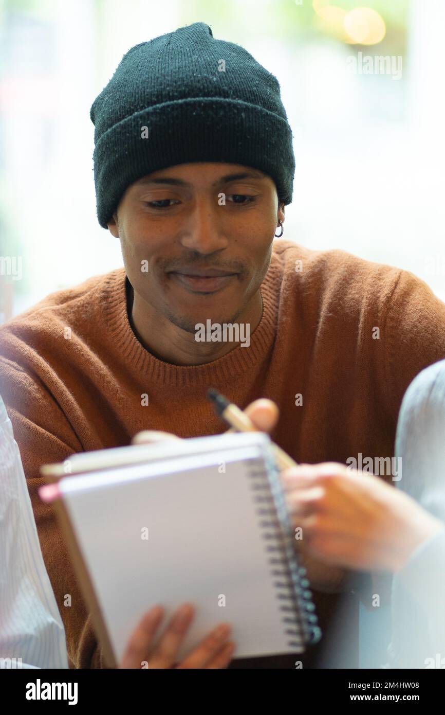 Collègues travaillant ensemble dans un espace de travail conjoint. Un gars à la peau sombre avec une casquette noire et un pull. Fille avec un stylo dans sa main montre quelque chose sur le Banque D'Images