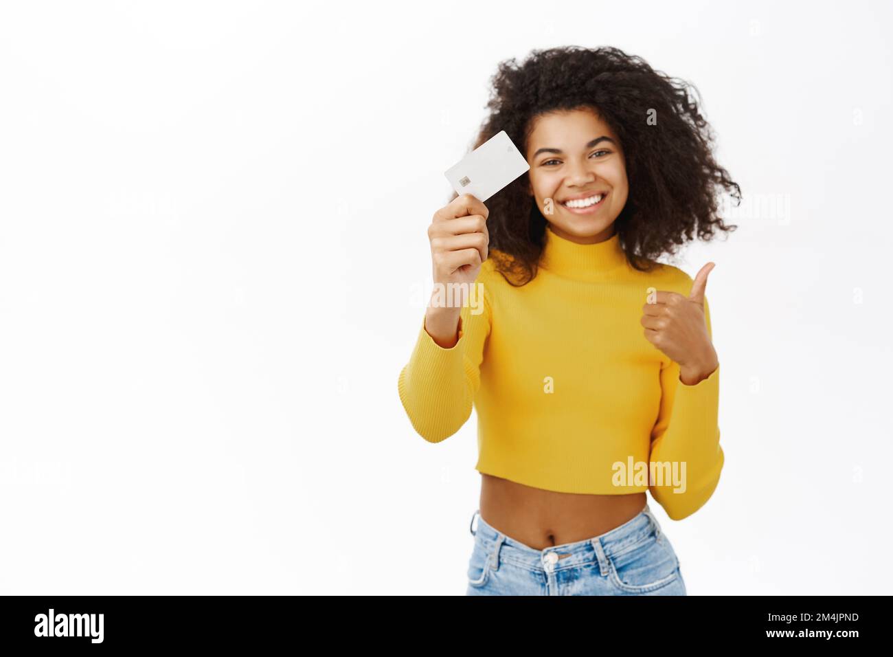 Souriant Black Girl montre sa carte de crédit, l'étudiant ID, fait le pouce vers le haut geste, se tient sur fond blanc Banque D'Images