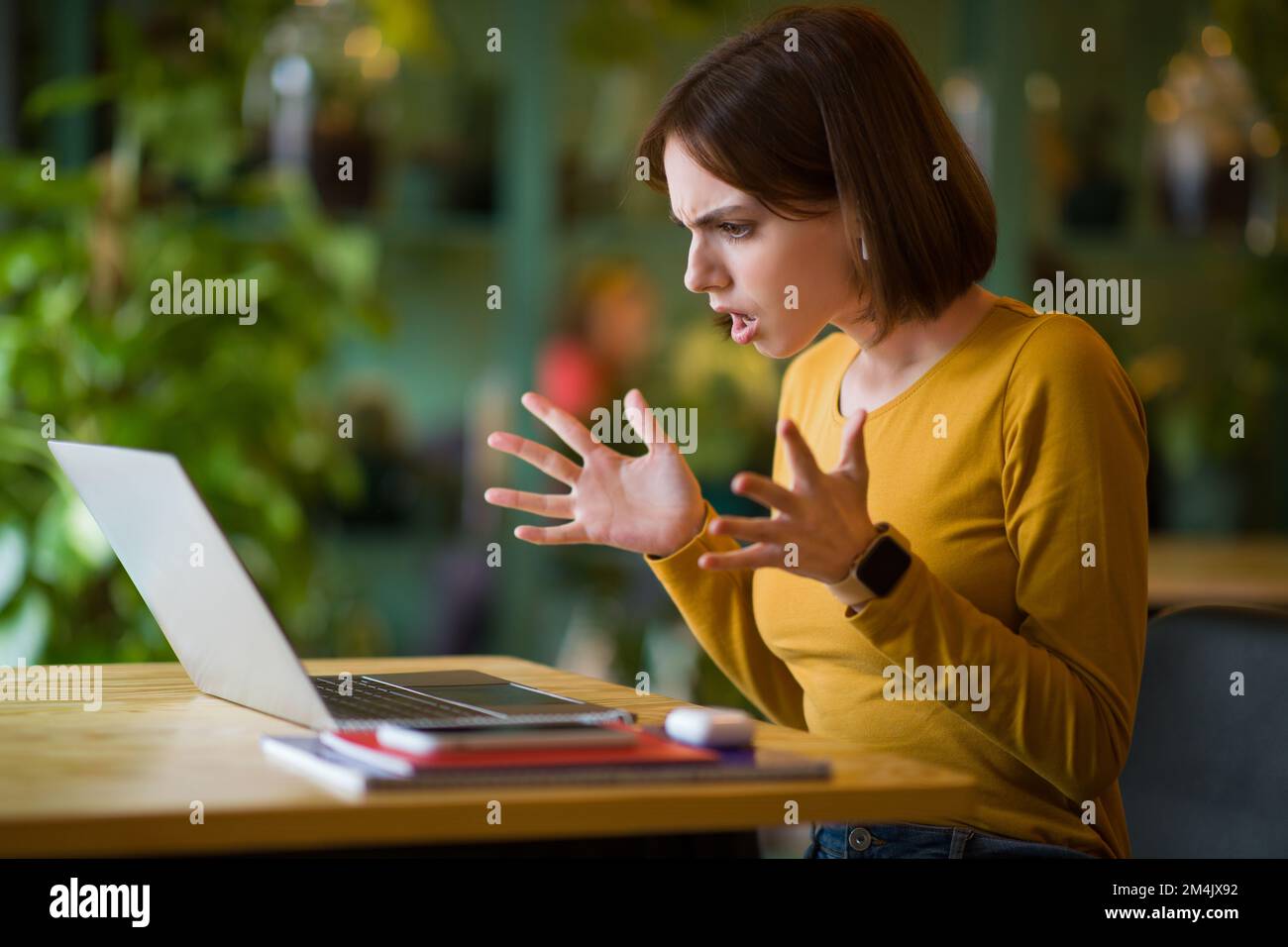 Jeune femme en colère assise dans un café, travaillant en ligne sur un ordinateur portable Banque D'Images