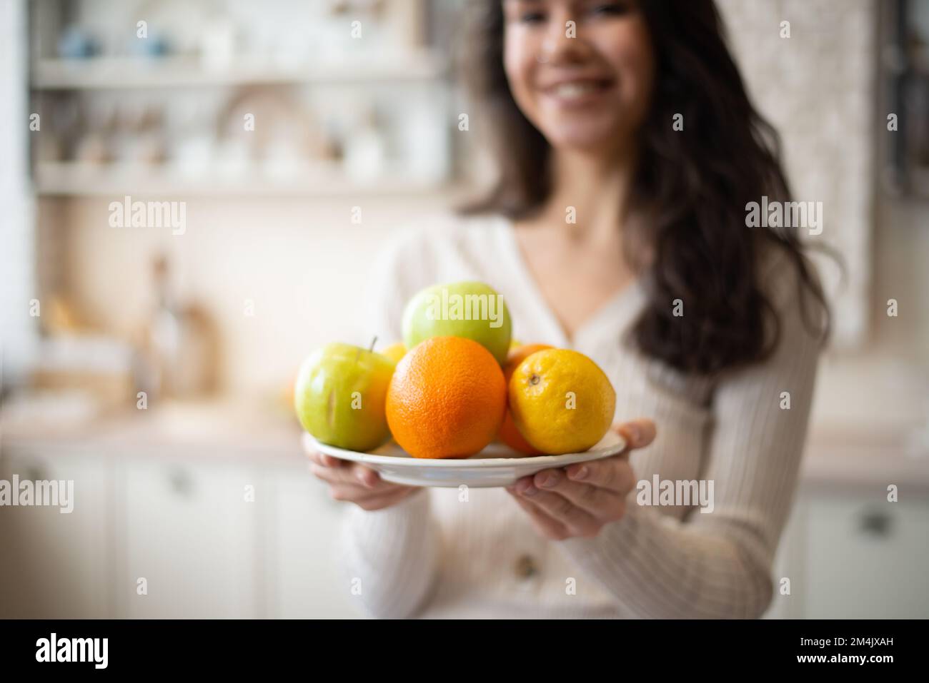 Jeune femme tenant une assiette avec des pommes de fruits frais et des oranges, debout dans l'intérieur de la cuisine, foyer sélectif, espace libre Banque D'Images